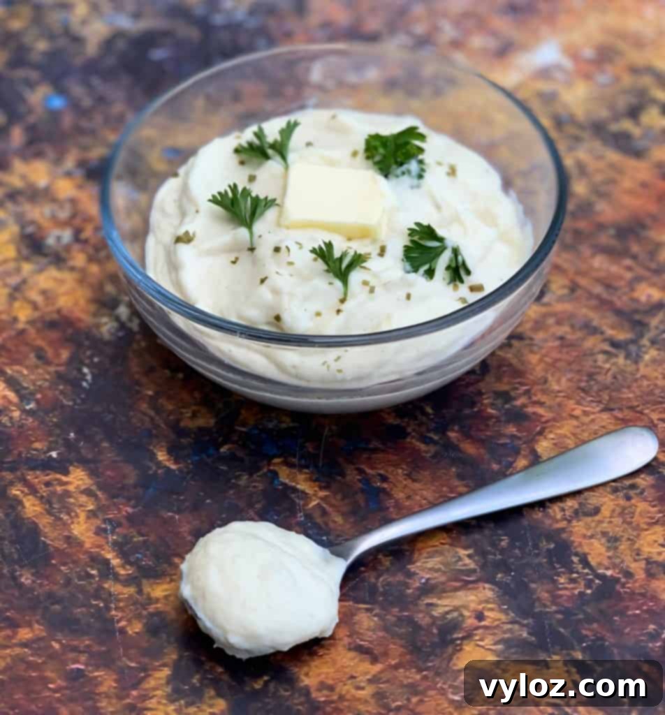 Keto cauliflower mash in a glass bowl with a pat of butter, fresh parsley, and a spoon