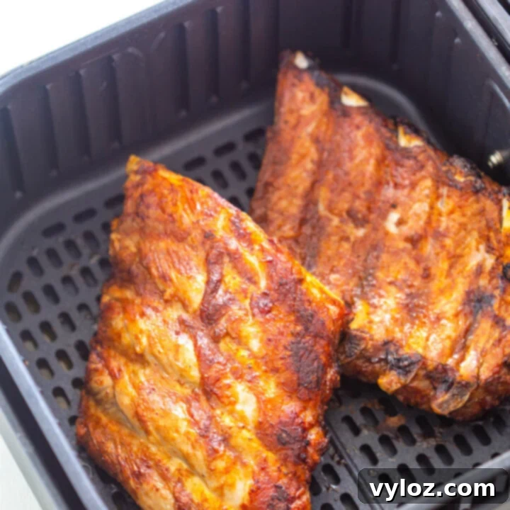Cooked ribs in an air fryer basket, glazed with BBQ sauce