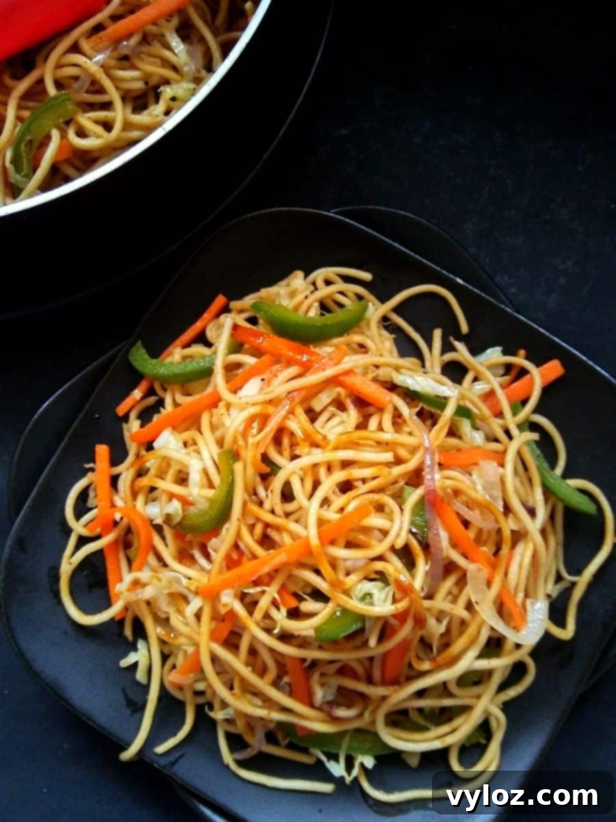 A generous serving of vegan vegetable chow mein, garnished with green onions and sesame seeds, presented in a bowl.
