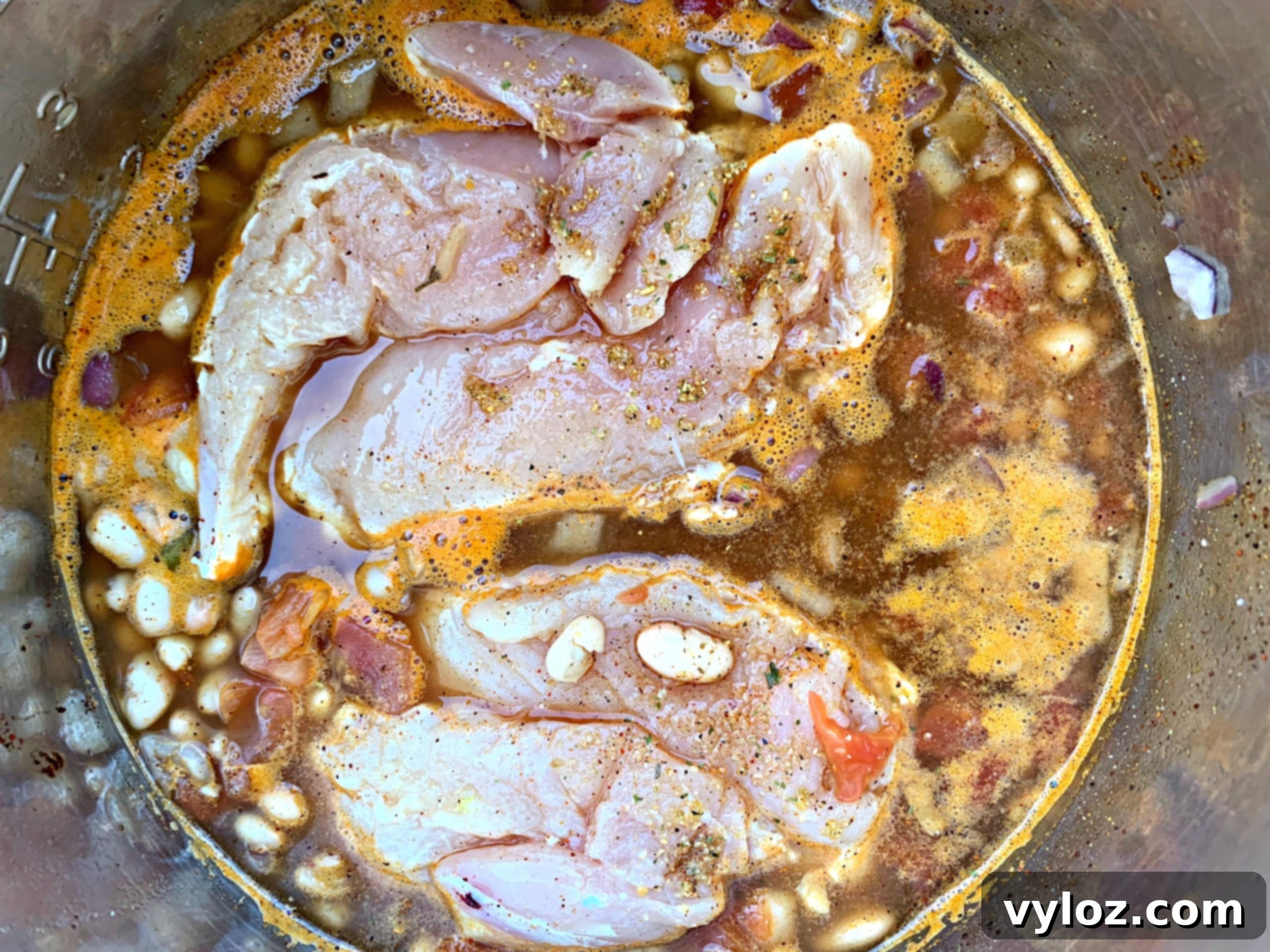 Raw chicken breasts, white beans, and diced tomatoes in an Instant Pot before cooking.