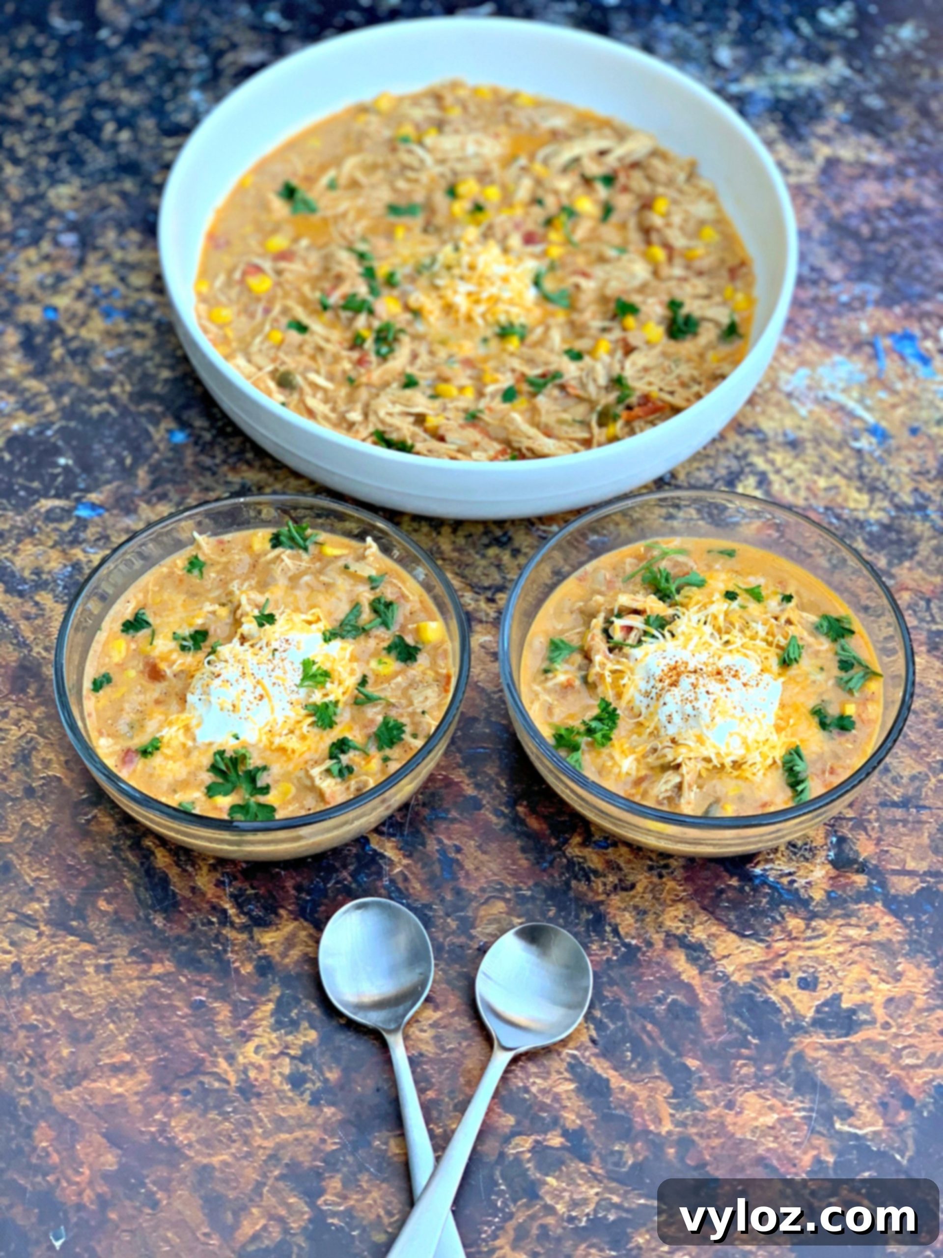 Three bowls of Instant Pot white chicken chili, each topped with cheese and fresh herbs, arranged on a wooden board.