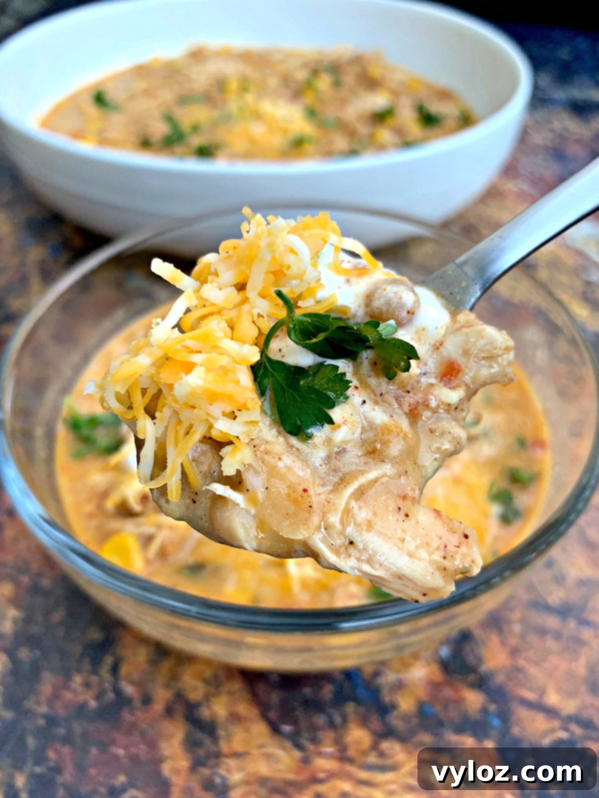 A close-up of a spoon scooping creamy white chicken chili from a bowl, highlighting its texture and ingredients.
