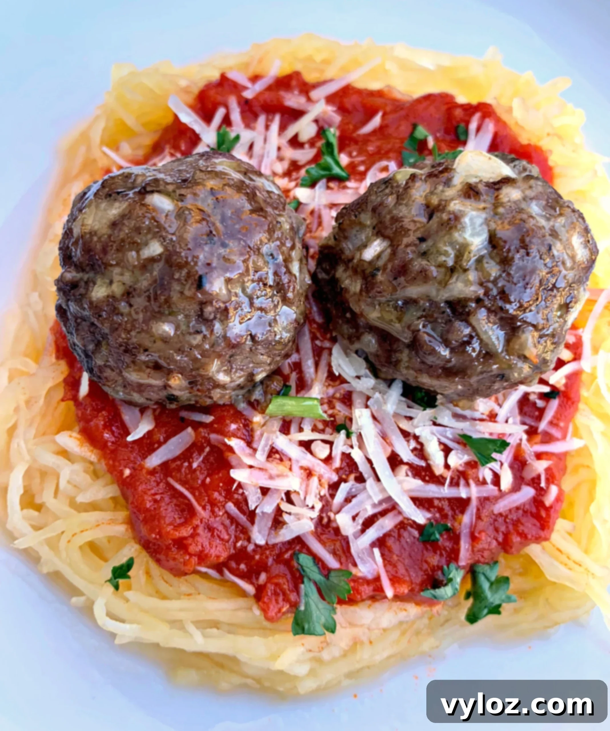 Delicious spaghetti squash marinara with perfectly cooked meatballs, garnished with fresh herbs, served in a clean white bowl.