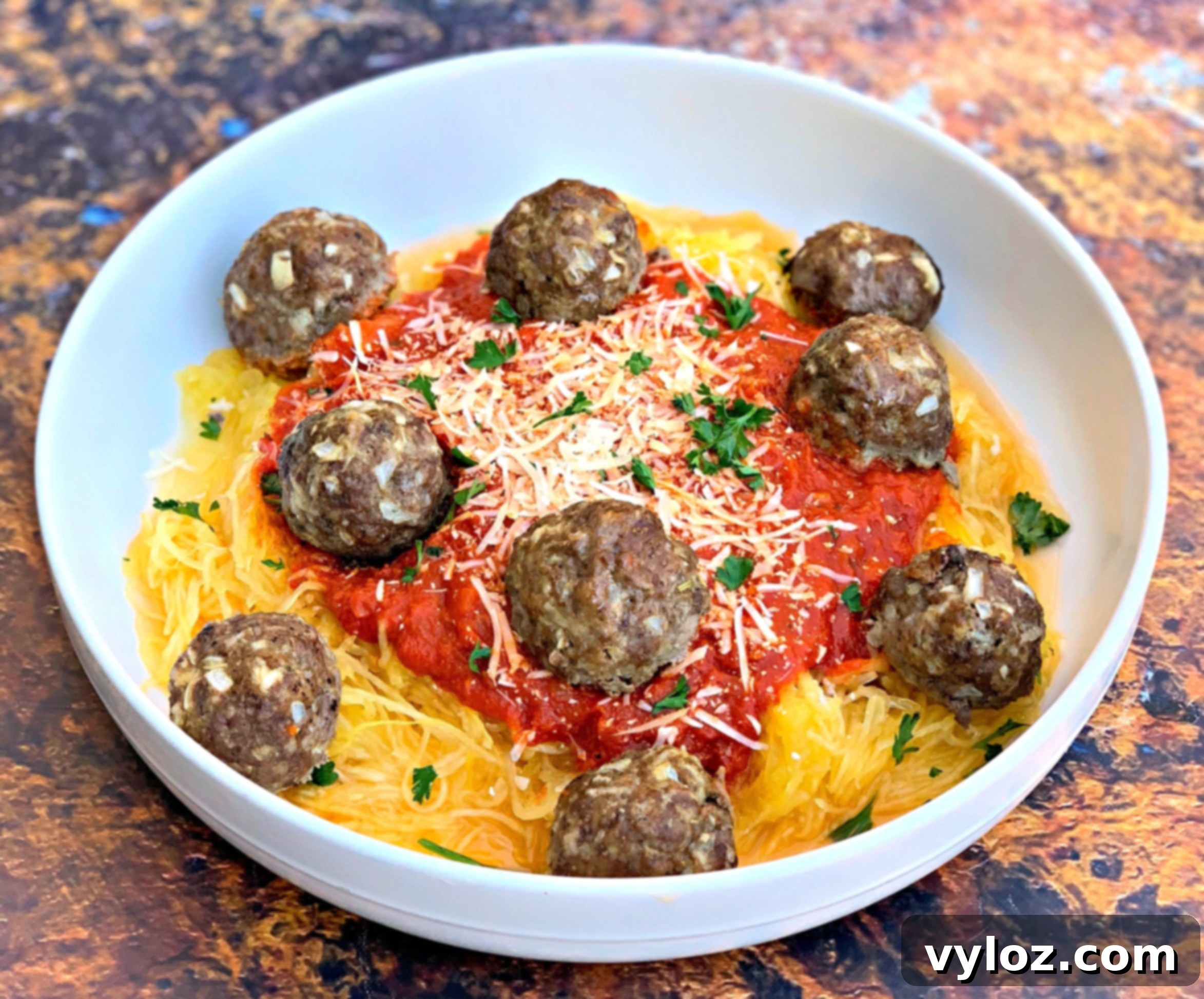 A beautiful close-up shot of a single serving of spaghetti squash marinara with tender meatballs, artfully garnished with fresh basil or parsley, presented in an elegant white bowl.