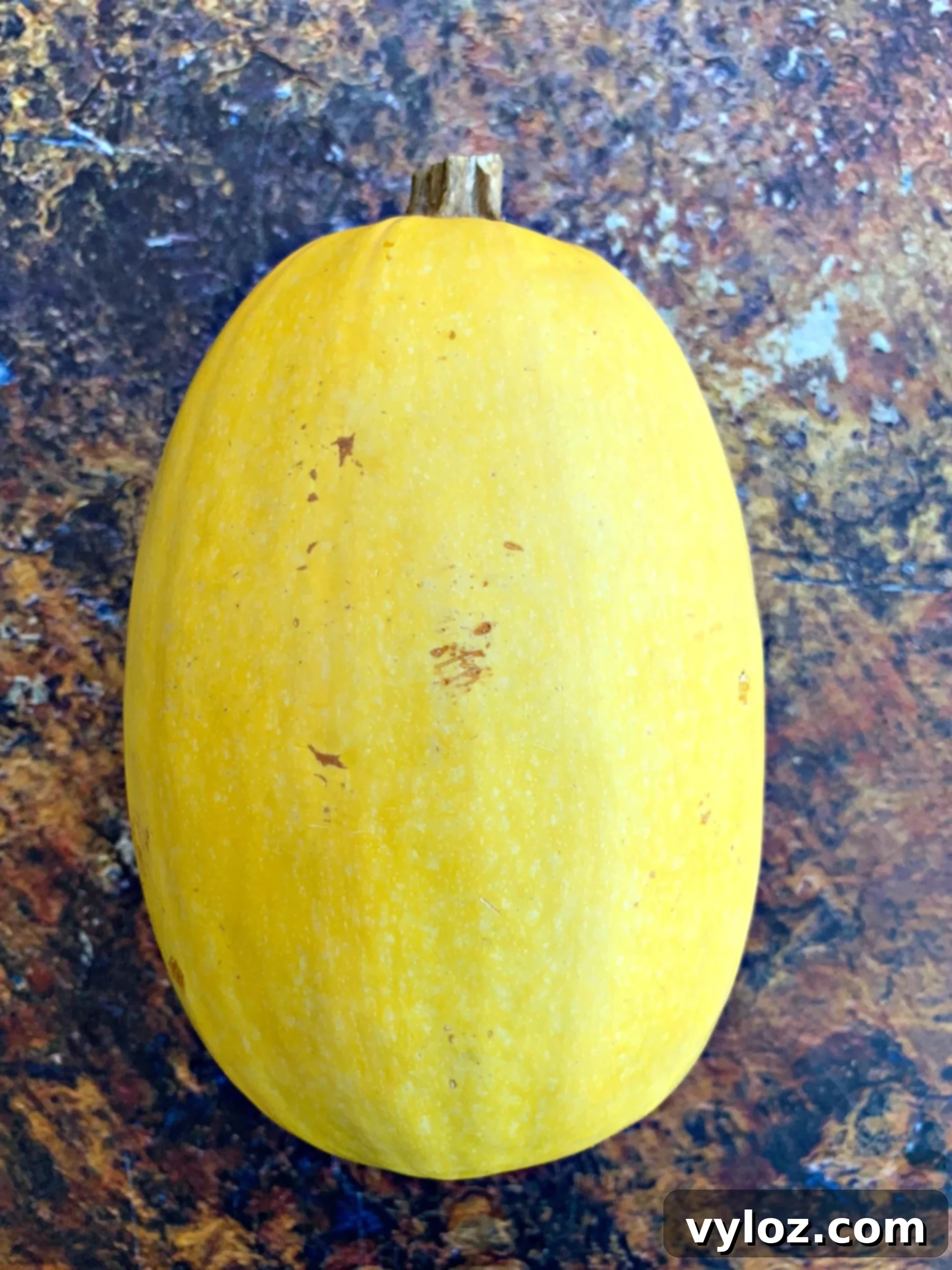 A fresh, uncut spaghetti squash resting on a rustic wooden cutting board, showcasing its vibrant yellow skin and preparing for its culinary transformation.