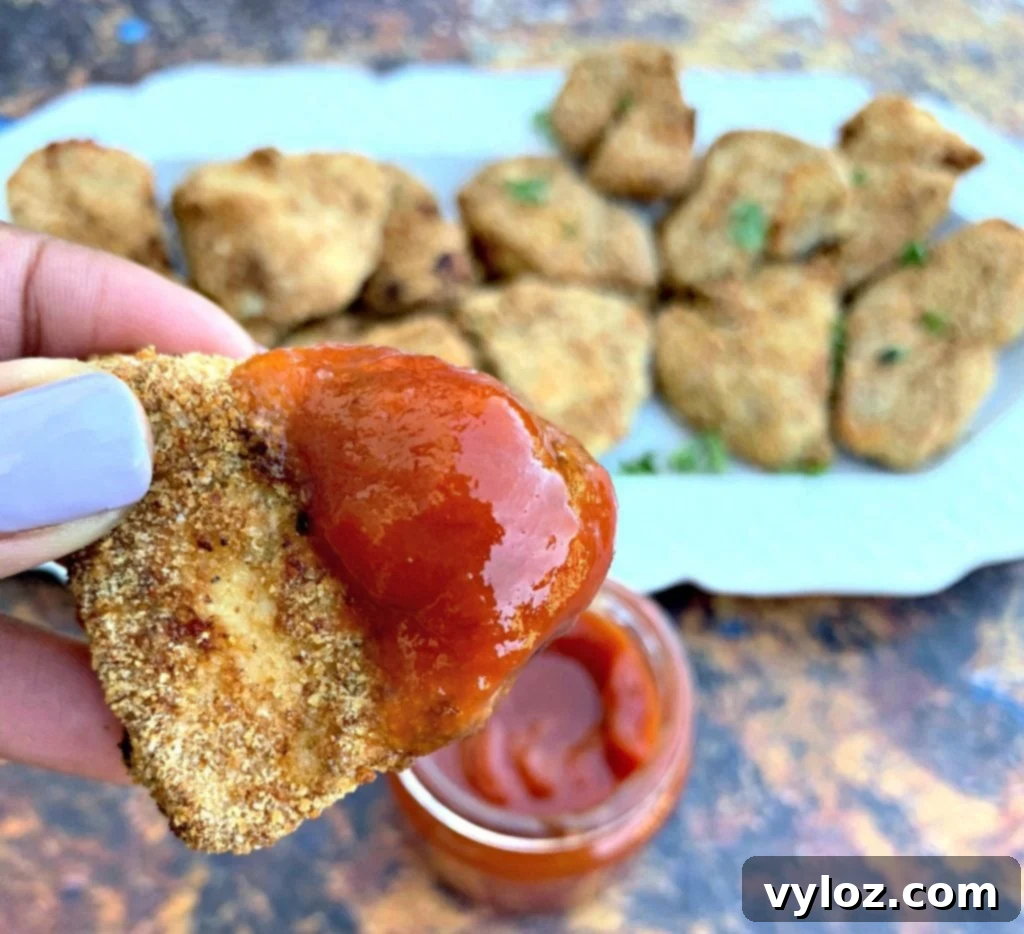 Crispy Air Fryer Chicken Nuggets 10 Air fryer chicken nuggets on a white plate with ketchup and a side of french fries