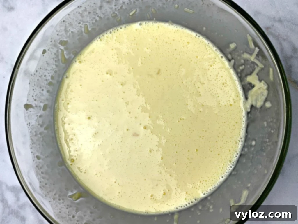 Whisked eggs, heavy whipping cream, and shredded cheese in a bowl, prepared for the casserole.