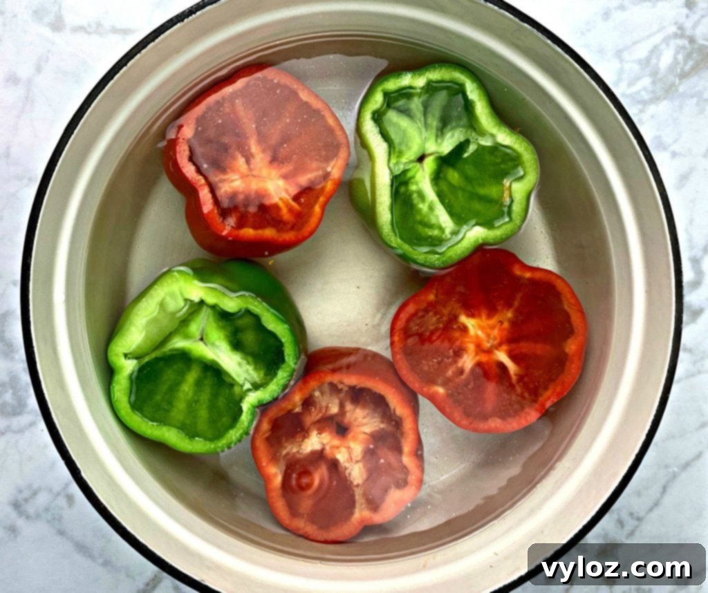 Bright red and green bell peppers boiling in a large pot of water on the stove, a key step in preparing tender stuffed peppers.