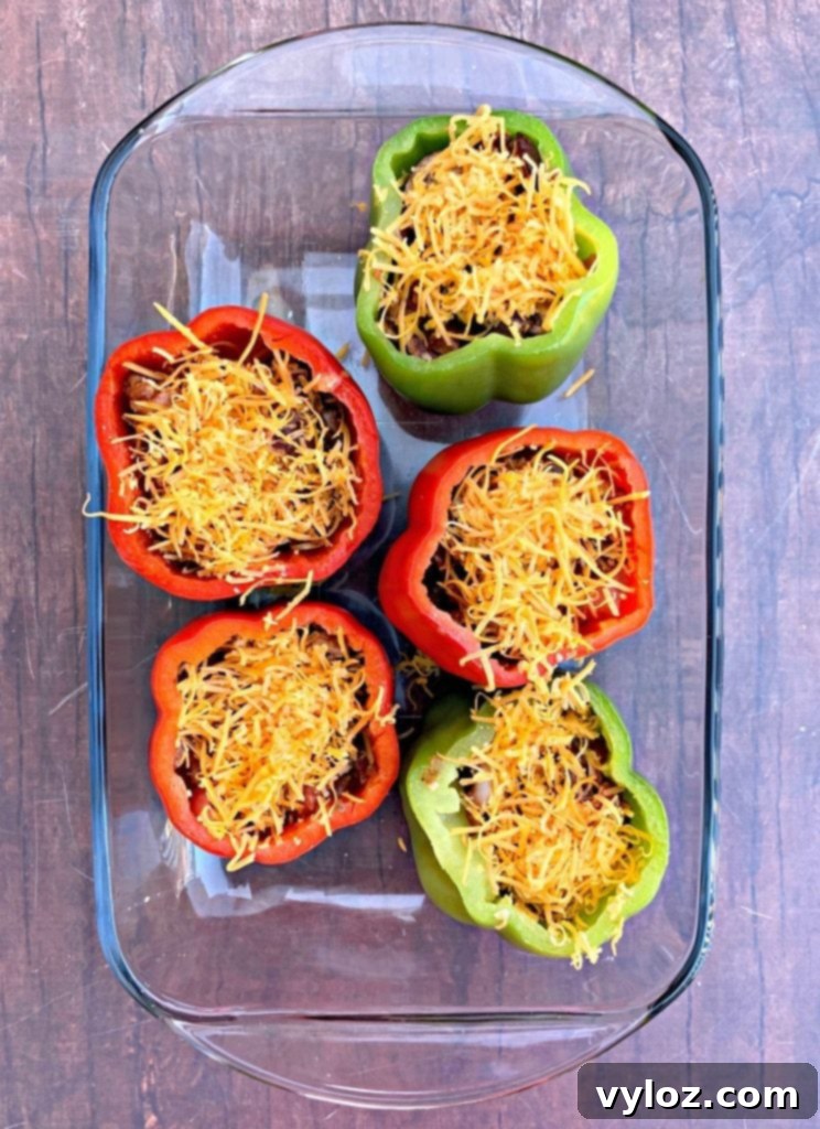 A glass baking dish filled with keto low-carb bacon, mushroom, and cheese stuffed peppers, ready to be baked.