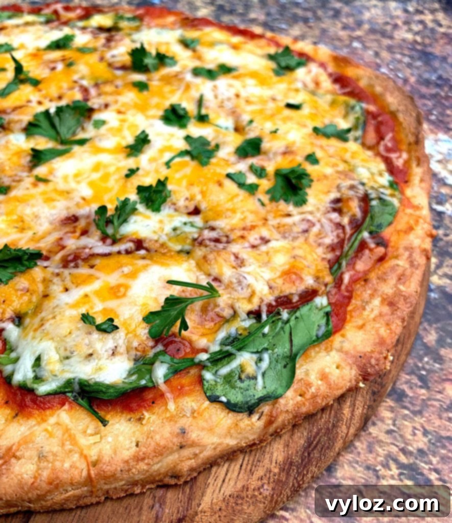 Fully assembled keto pepperoni pizza with marinara, pepperoni, and a medley of cheeses and spinach, ready for its final bake.