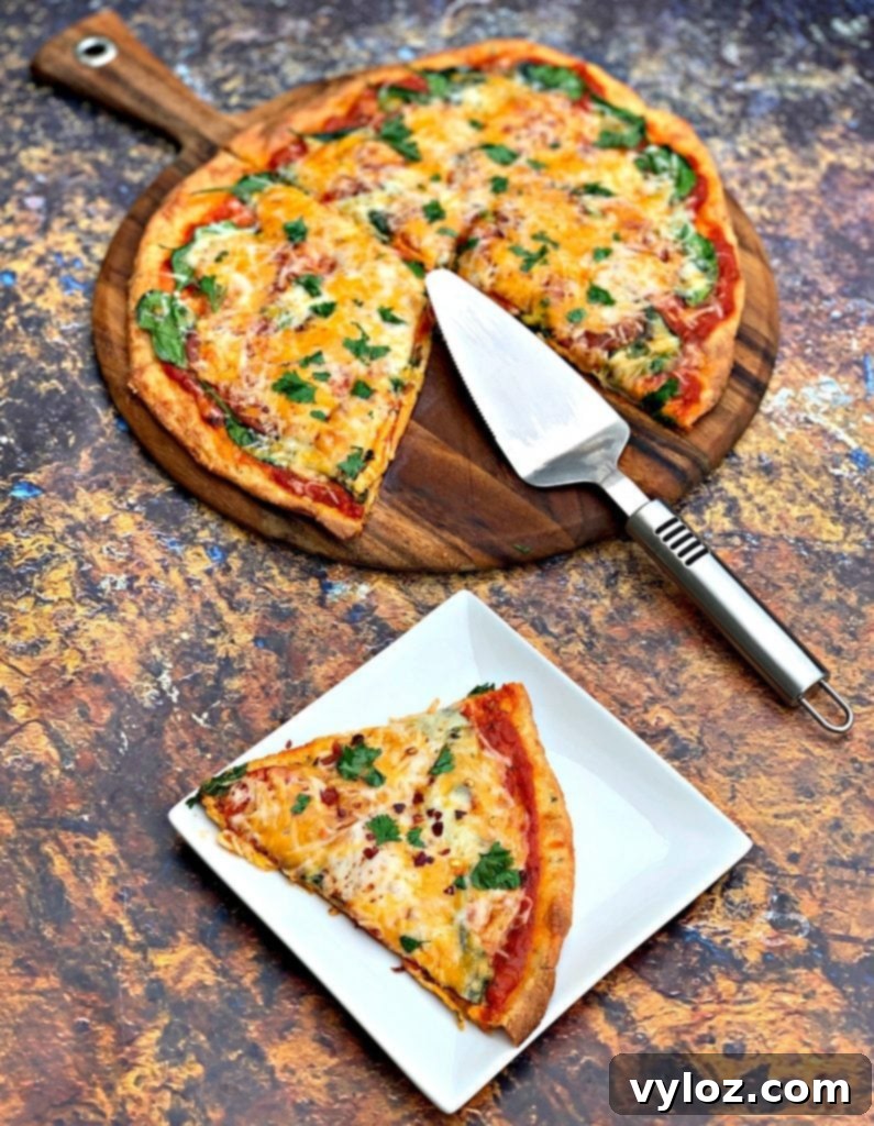 A perfectly baked slice of keto pepperoni pizza on a white plate, with the rest of the pizza visible on the pan in the background.