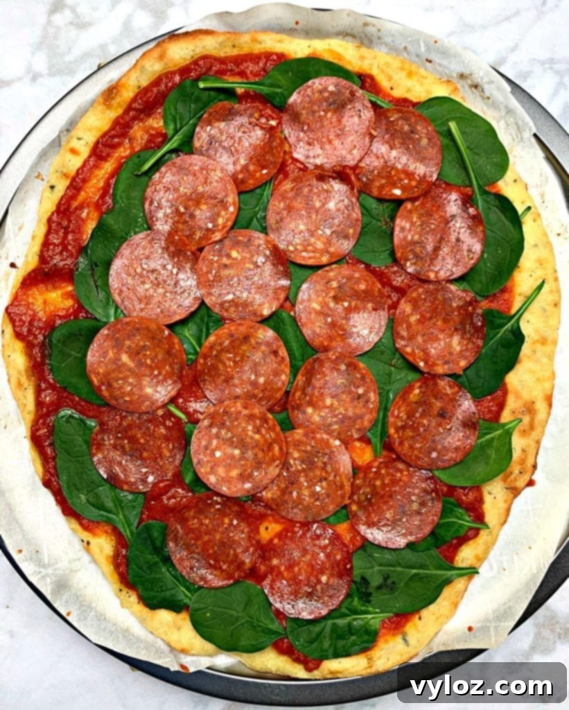 Keto pepperoni pizza on a pizza pan with marinara sauce and evenly distributed pepperoni slices, ready for cheese.