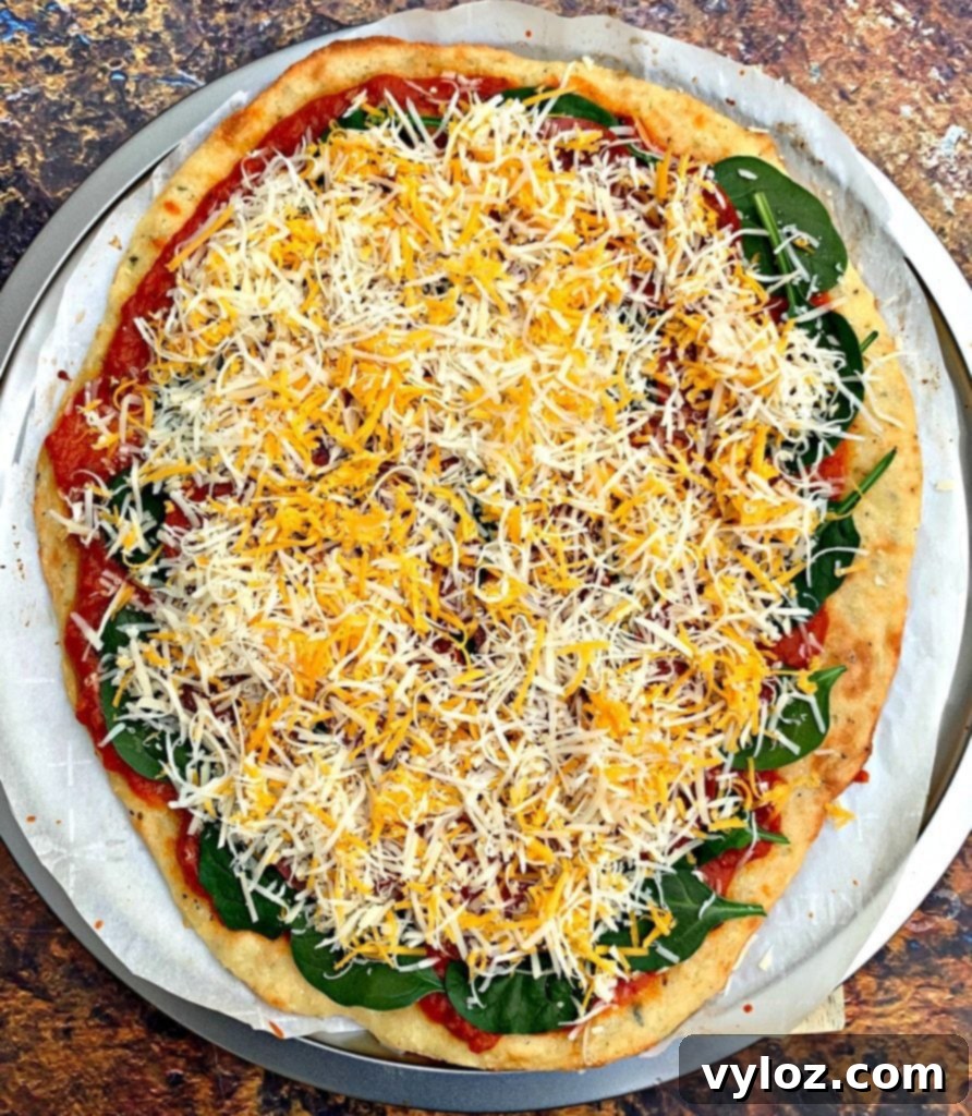 Keto pepperoni pizza on a pizza pan fully topped with marinara, pepperoni, and a generous layer of shredded cheese.