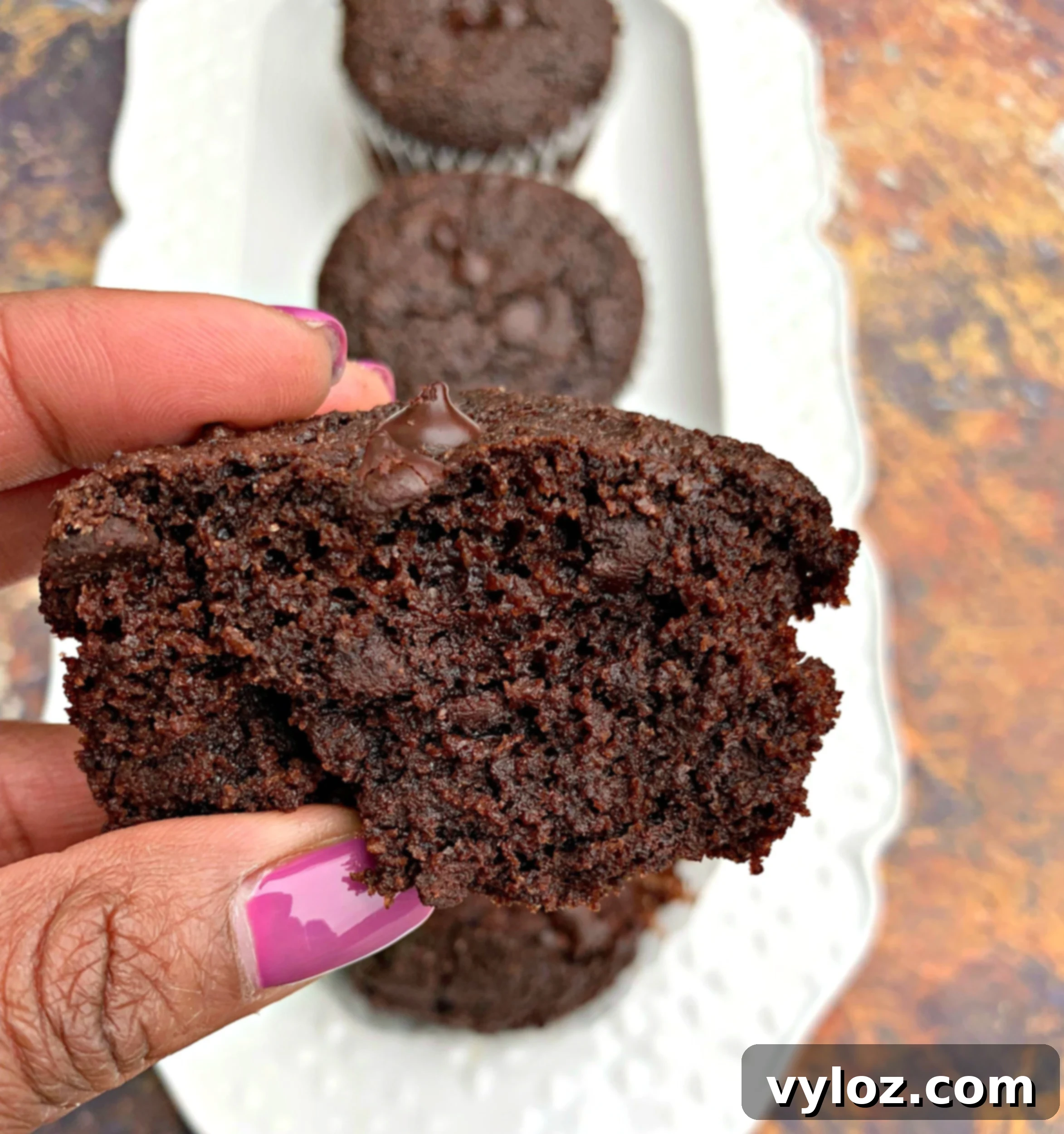person holding keto low carb chocolate muffins over muffins on a white plate