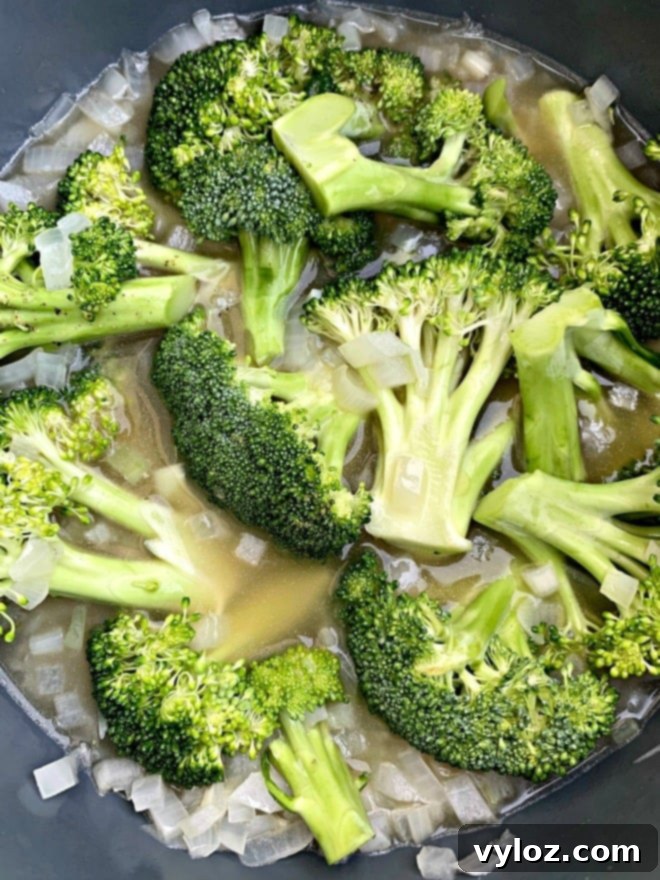 Sautéed broccoli and onions simmering in an Instant Pot, forming the base of the delicious cheddar soup.