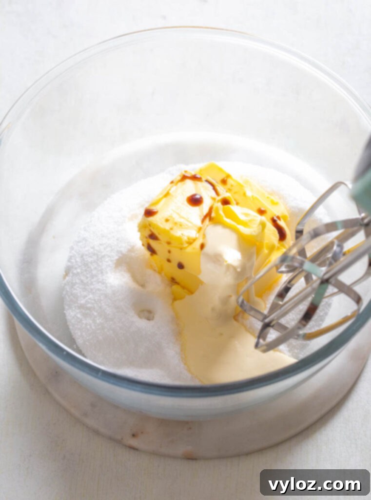 Room temperature butter and powdered sweetener being creamed together in a glass bowl with a hand mixer, essential for fluffy frosting.