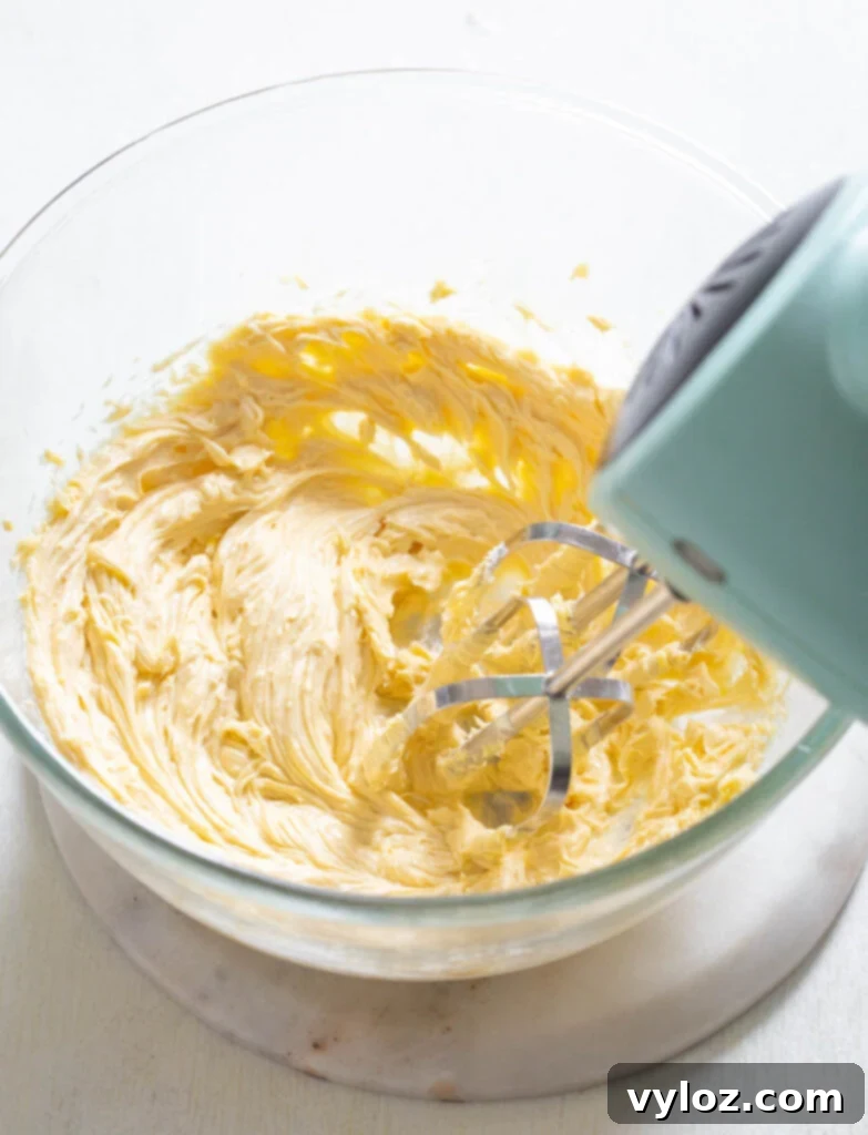 Luxuriously fluffy sugar-free buttercream frosting in a glass bowl, whipped to perfection with a hand mixer, ready to elevate any dessert.