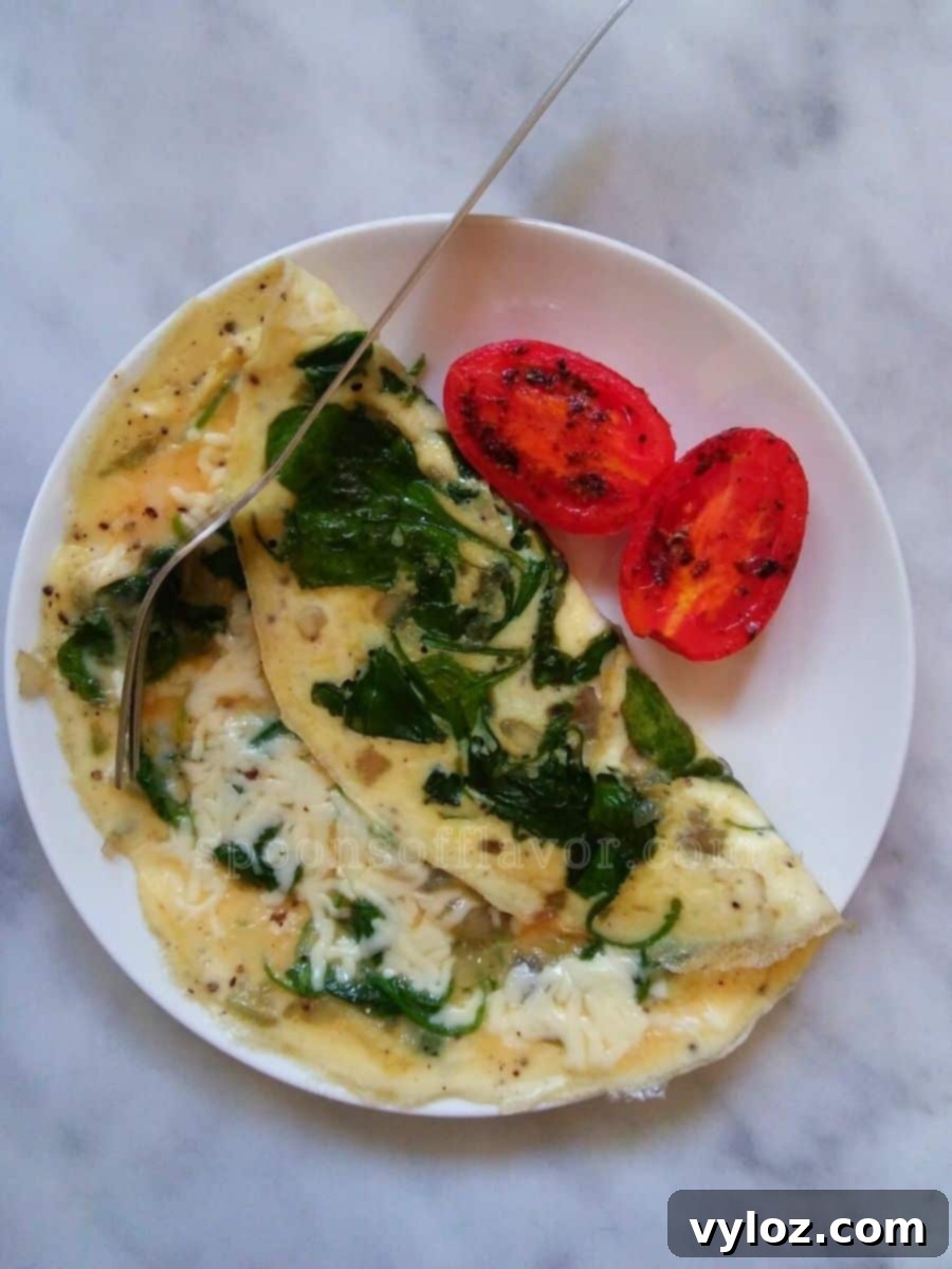 Quick and Delicious Cheesy Spinach Omelet 2 Image showing spinach, eggs and cheese omelet served with roasted tomatoes.