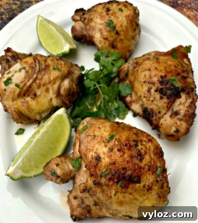 Close-up of air fryer keto low carb cilantro lime chicken thighs on a white plate with lime and fresh cilantro, garnished with fresh herbs