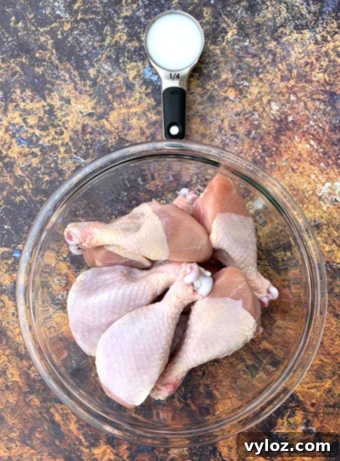 Buttermilk and raw chicken drumsticks soaking in a glass bowl.