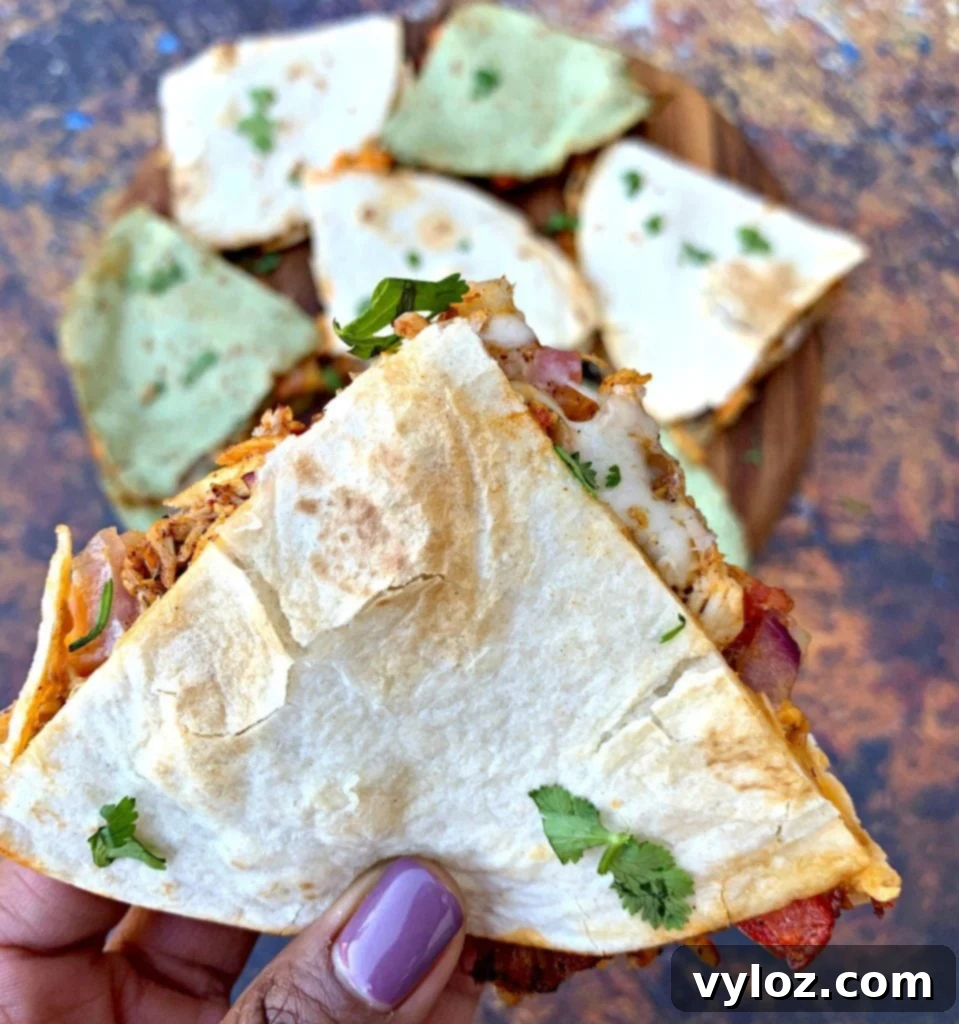 A person holding a delicious segment of air fryer chicken quesadilla, showing the warm, cheesy filling