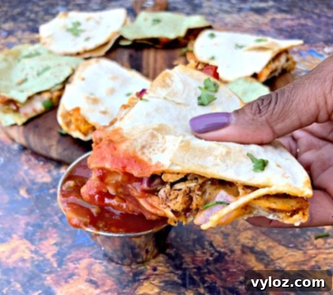 A person holding an air fryer chicken quesadilla wedge, perfectly dipped into a bowl of fresh, vibrant salsa