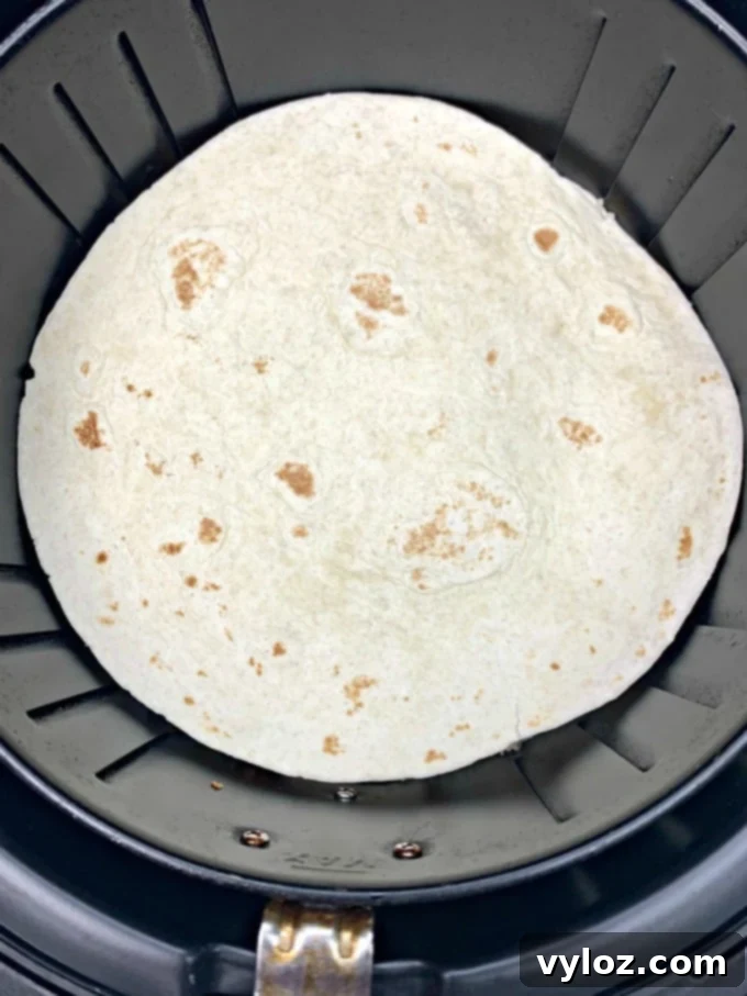 An air fryer chicken quesadilla cooking inside the air fryer basket, showing the top tortilla held down by a wire rack