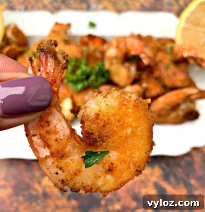 A hand holding a piece of crispy keto low carb breaded shrimp, emphasizing its perfect golden-brown texture