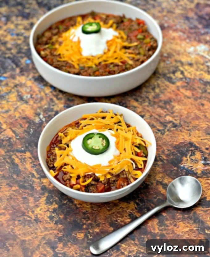 Two white bowls filled with flavorful keto beef chili, generously topped with shredded cheese, ready to be served.