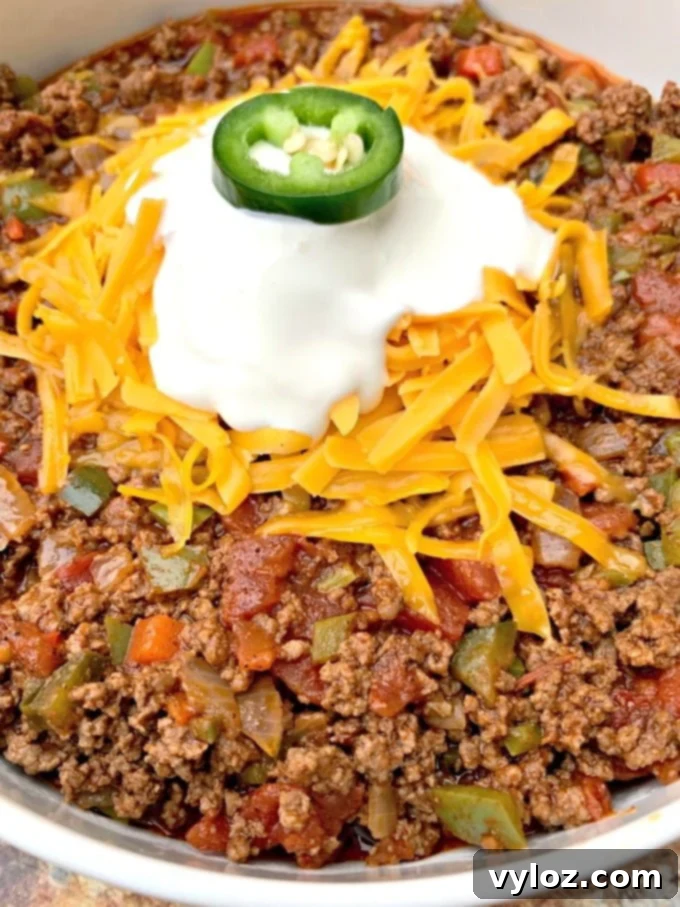 Detailed close-up of keto beef chili, showcasing its rich texture, garnished with a swirl of sour cream and a generous sprinkle of shredded cheese.