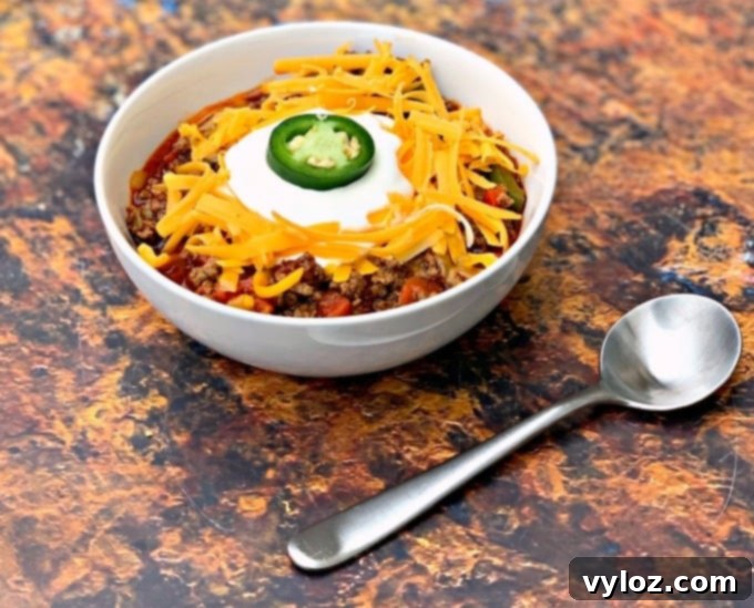 A wide shot of keto beef chili served in a white bowl, generously topped with shredded cheese and a dollop of sour cream, ready for enjoyment.
