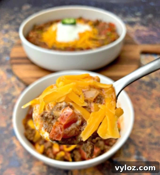 A spoon laden with rich keto beef chili, garnished with melted shredded cheese, highlighting its hearty texture and appealing warmth.