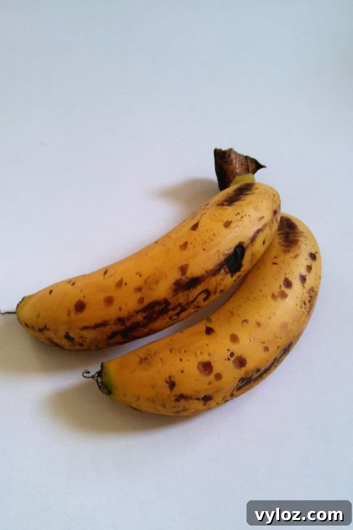 Two ripe bananas with noticeable black spots on their skins, indicating ideal ripeness for a banana milkshake.
