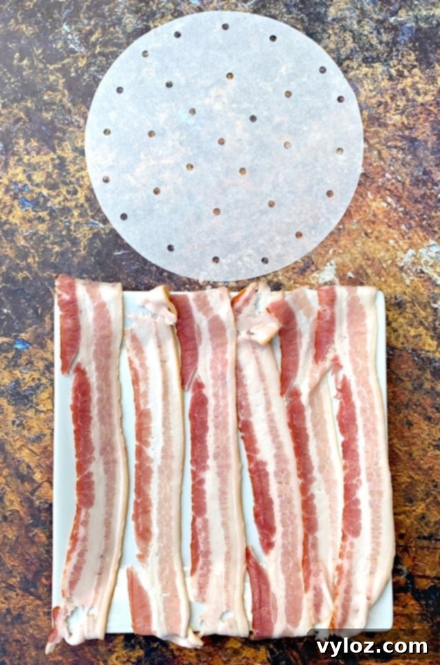 Uncooked bacon slices laid out on air fryer parchment paper.