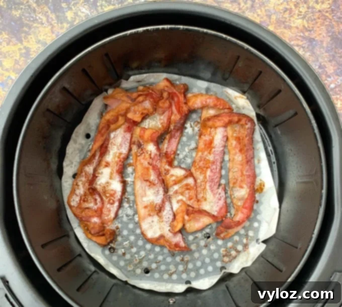 Perfectly cooked crispy bacon in an air fryer basket on parchment paper.