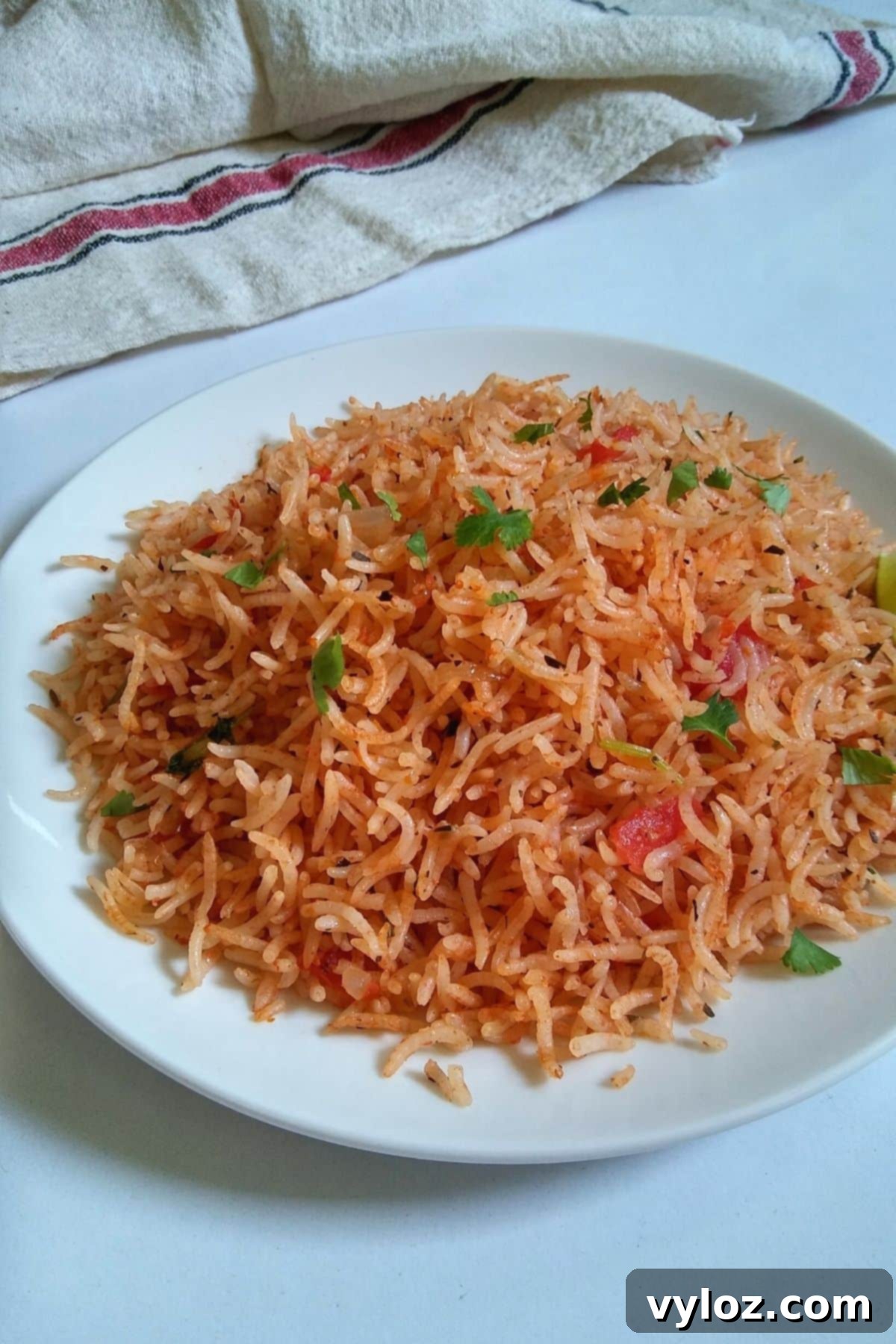 Vibrant orangish red rice served on a white plate along with two lime wedges, ready to be enjoyed as a perfect side dish.