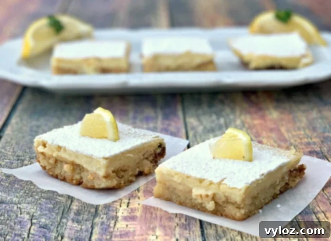 Simple Zesty Keto Lemon Bars 2 Two keto lemon bars on parchment paper with three lemon bars on a white plate