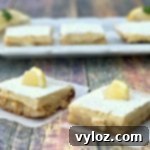 Simple Zesty Keto Lemon Bars 11 Two keto lemon bars on parchment paper with three lemon bars on a white plate