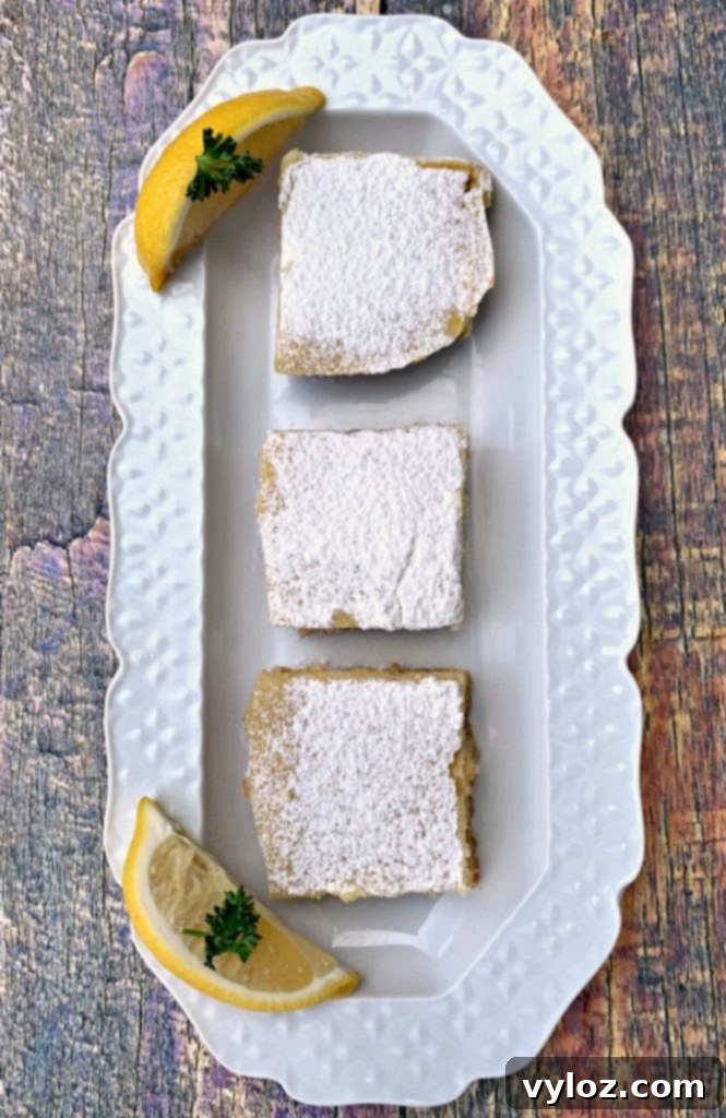 Simple Zesty Keto Lemon Bars 8 Three keto lemon bars on a white plate topped with confectioner's sugar