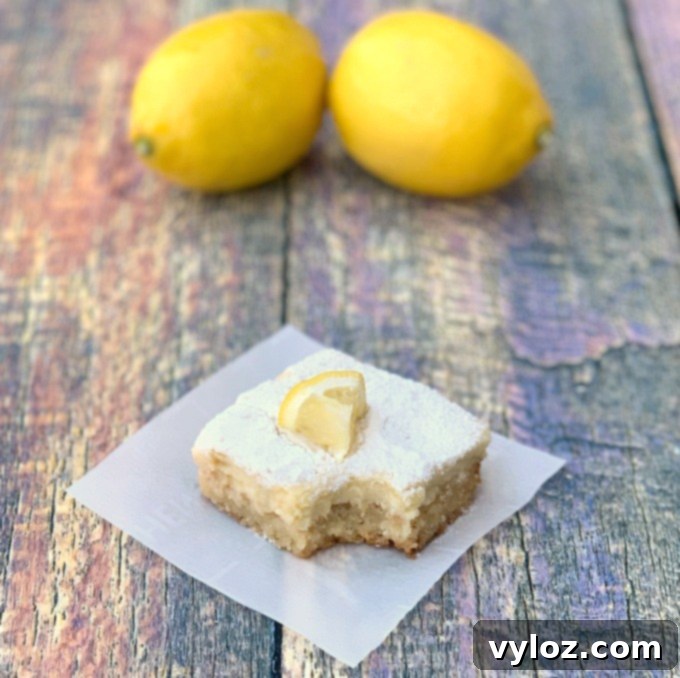 Simple Zesty Keto Lemon Bars 10 Keto lemon bar on parchment paper that has been bitten with two lemons