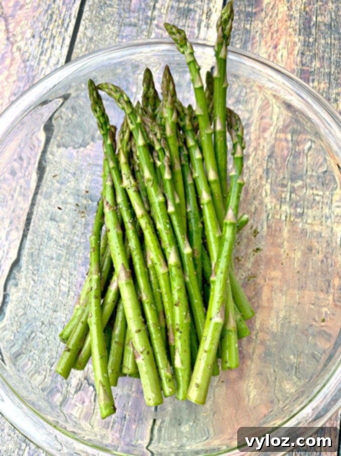 Raw asparagus drizzled with olive oil in a glass bowl