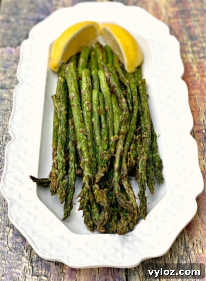 Perfectly air-fried roasted asparagus served on a white plate with lemon wedges