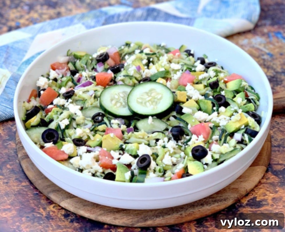 Fresh Keto Zucchini Noodle Pasta Salad in a white bowl with colorful tomatoes, olives, cucumbers, feta cheese, and red onions, showcasing healthy ingredients.