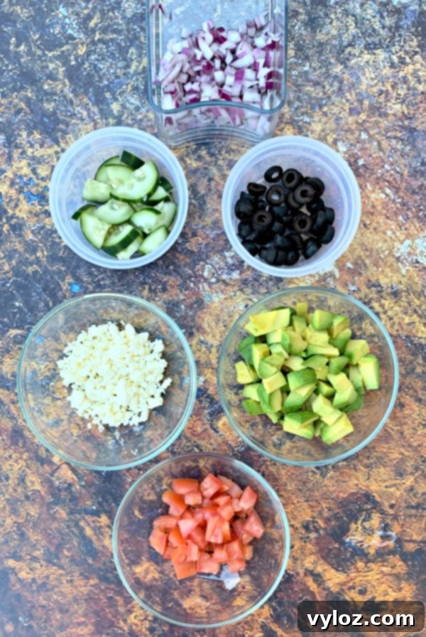 Various fresh ingredients for Keto Zucchini Noodle Pasta Salad laid out in separate bowls, including spiralized zucchini, tomatoes, olives, cucumbers, and red onions.