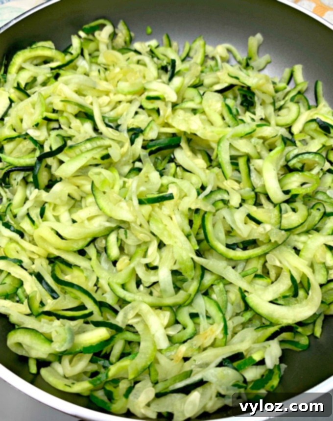 Zucchini noodles gently sautéing in a pan with olive oil, prepared for a healthy pasta salad.