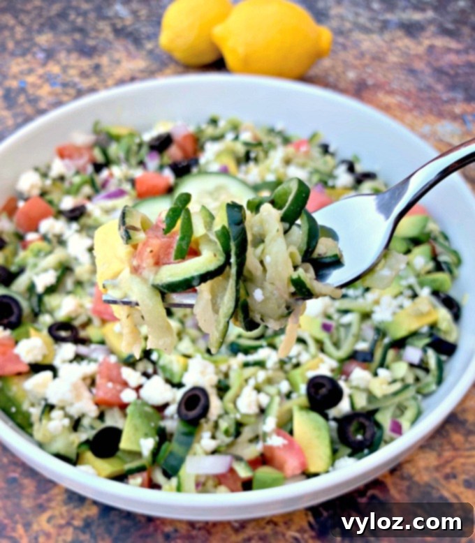 An overhead view of a fork serving a portion of Keto Zucchini Noodle Pasta Salad from a white bowl, highlighting its fresh ingredients.