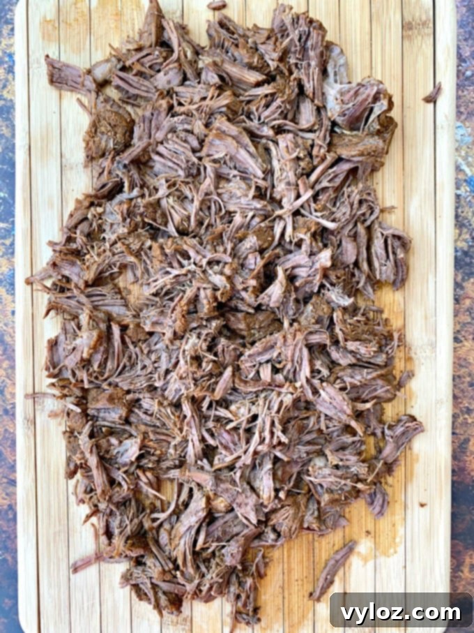 Instant Pot Chipotle Barbacoa Beef 7 Instant Pot keto low carb barbacoa beef garnished with fresh cilantro and lime wedges on a rustic cutting board