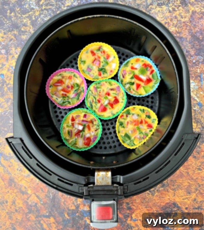 Uncooked keto-friendly, low-carb Air Fryer Egg Bites cups, filled with egg mixture and various ingredients, placed on a brown plate.