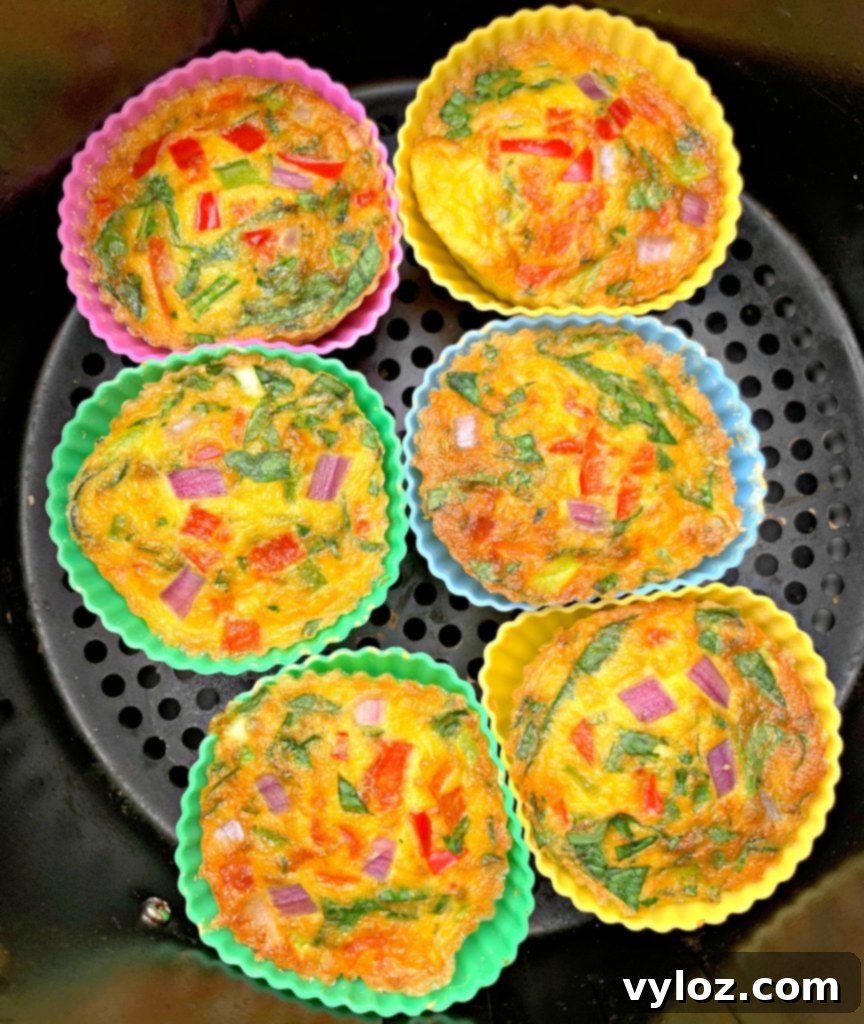 Freshly cooked keto-friendly, low-carb Air Fryer Egg Bites cups resting in the basket of an air fryer, golden and ready to serve.