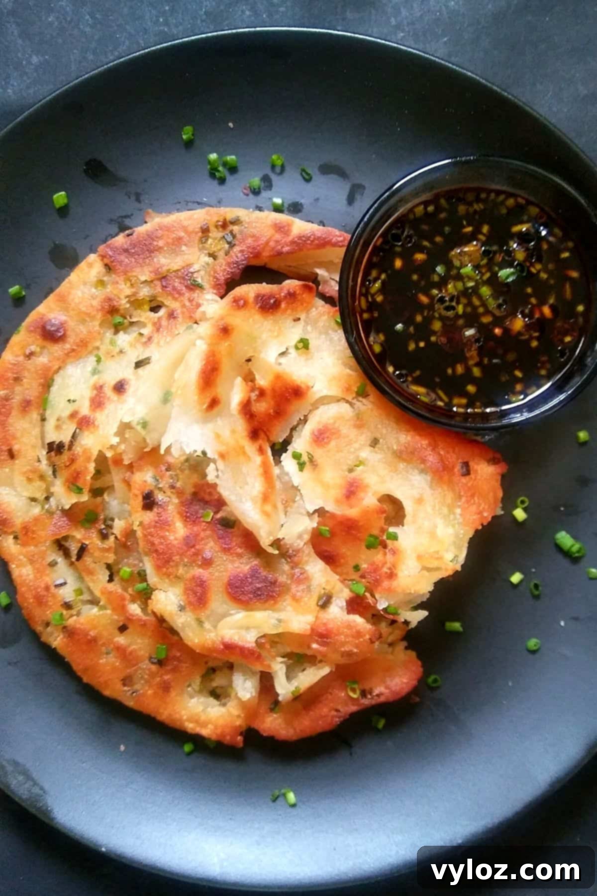 image showing scallion pancake served on a black plate with soy dipping sauce.